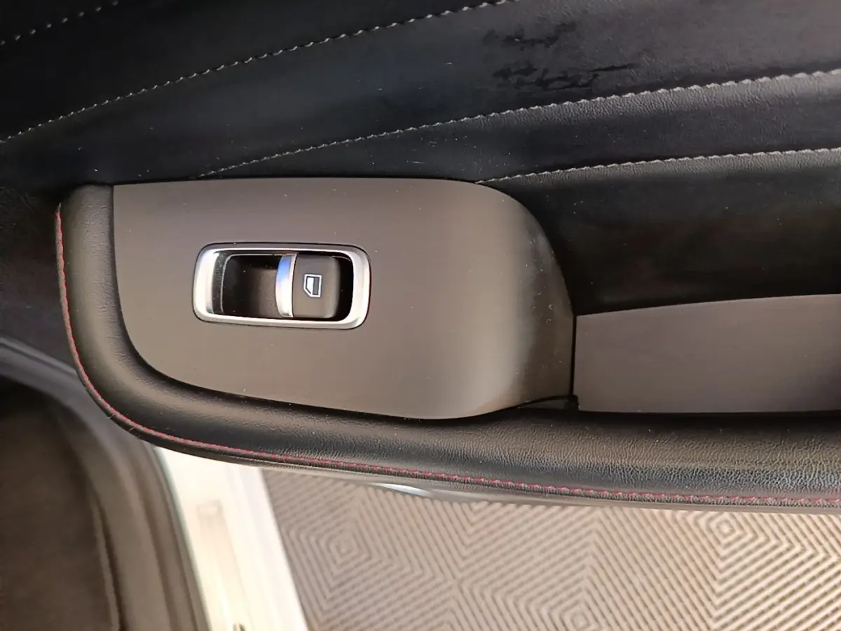 Détail de la commande de lève-vitre sur la porte intérieure noire avec surpiqûres rouges d’un MG MOTOR EHS blanc.