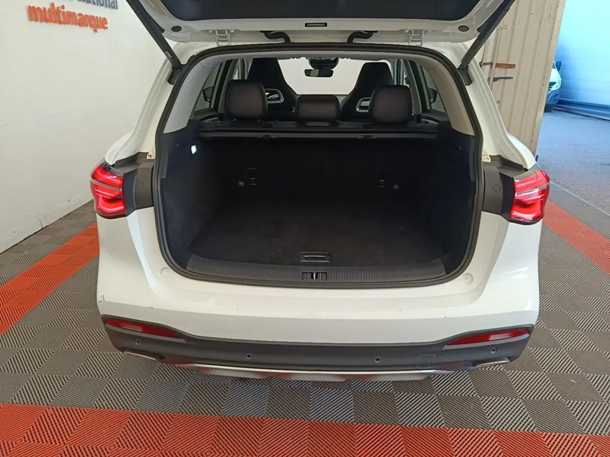 Vue arrière ouverte du coffre d’un MG MOTOR EHS blanc 2023, montrant l’espace de chargement et les feux arrière allumés.