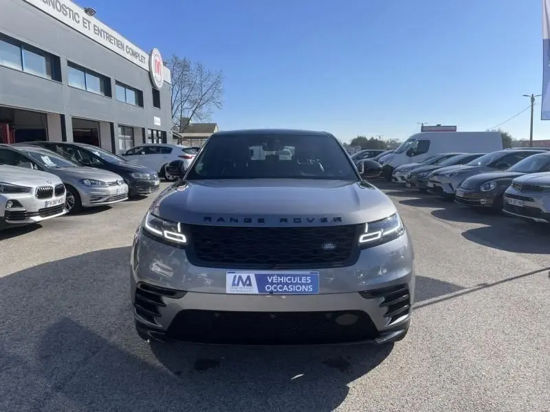 Vue frontale d'un Range Rover Velar gris métal 2020 avec phares LED allumés sur un parking extérieur.
