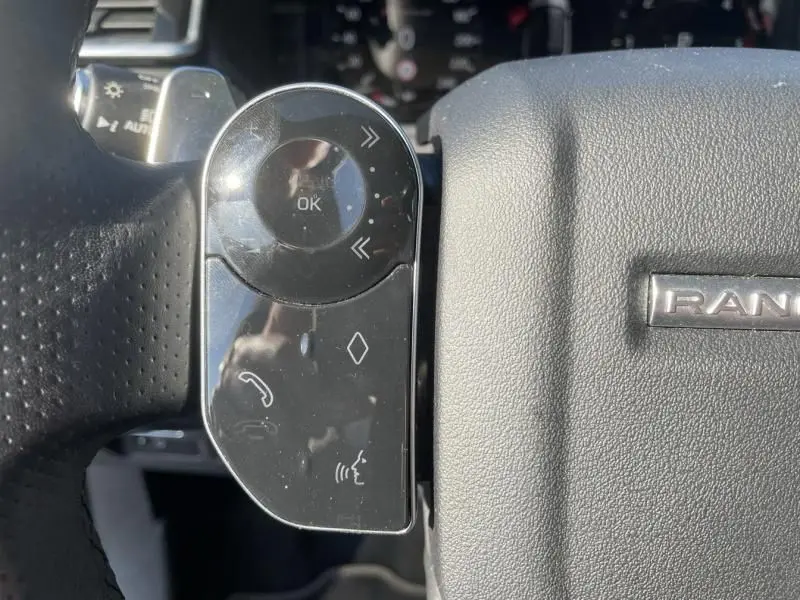 Gros plan sur les commandes gauche du volant gris métal du Range Rover Velar 2020, avec boutons multifonctions et logo partiel.