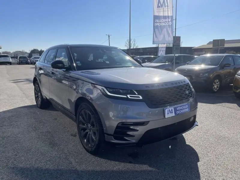 Vue 3/4 avant d'un Range Rover Velar gris métal 2020 avec calandre noire et jantes foncées sur parking.