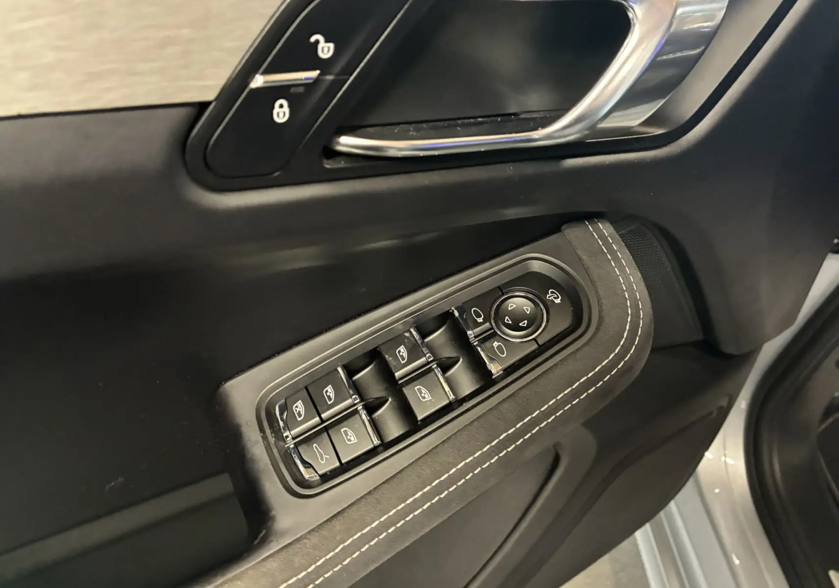 Gros plan sur la commande des vitres et la poignée de porte côté conducteur du Porsche Macan 3.0 360 GTS noir avec surpiqûres blanches.