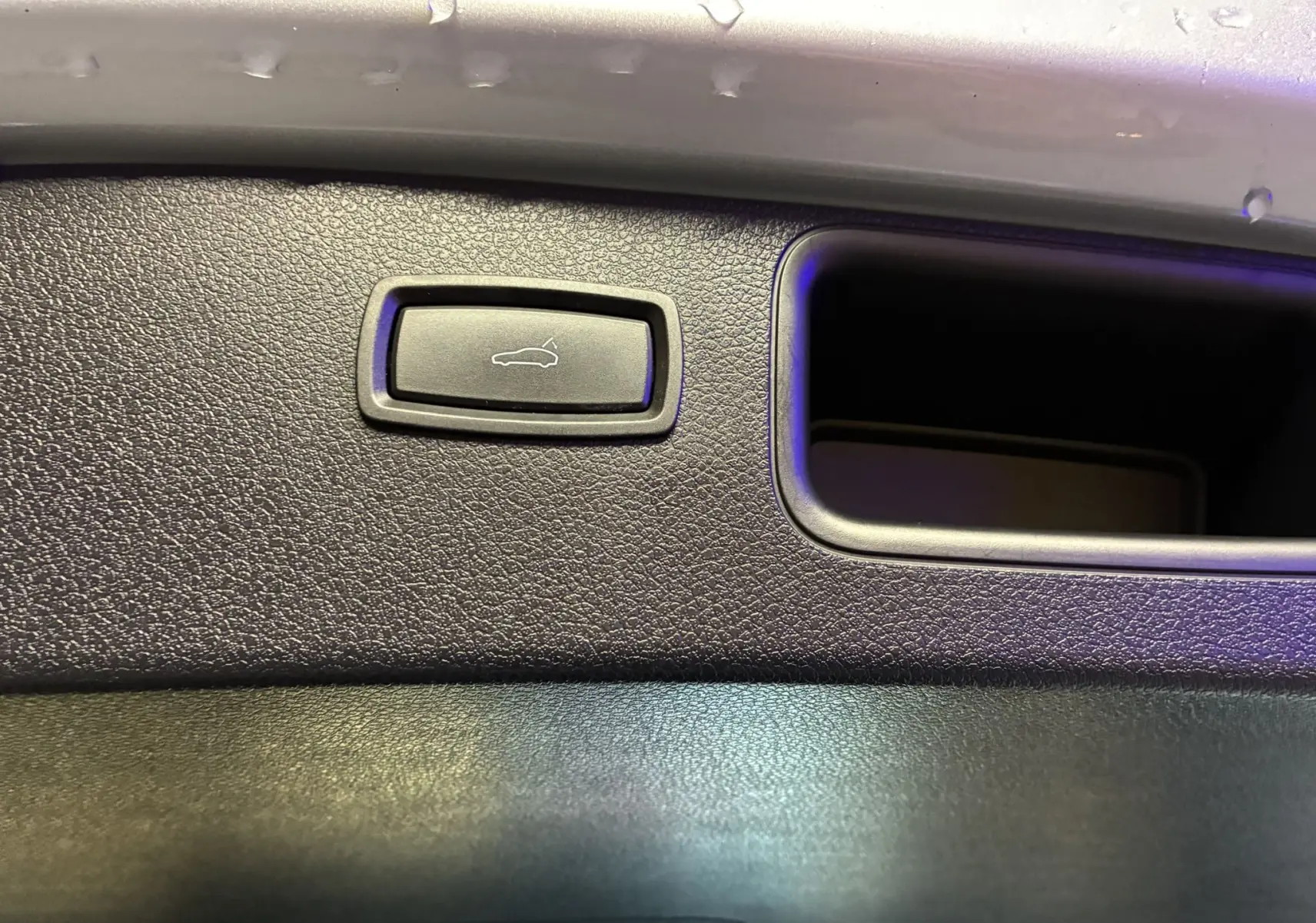 Gros plan sur le bouton d'ouverture du hayon intégré dans le panneau intérieur noir du coffre du Porsche Macan GTS 2017.