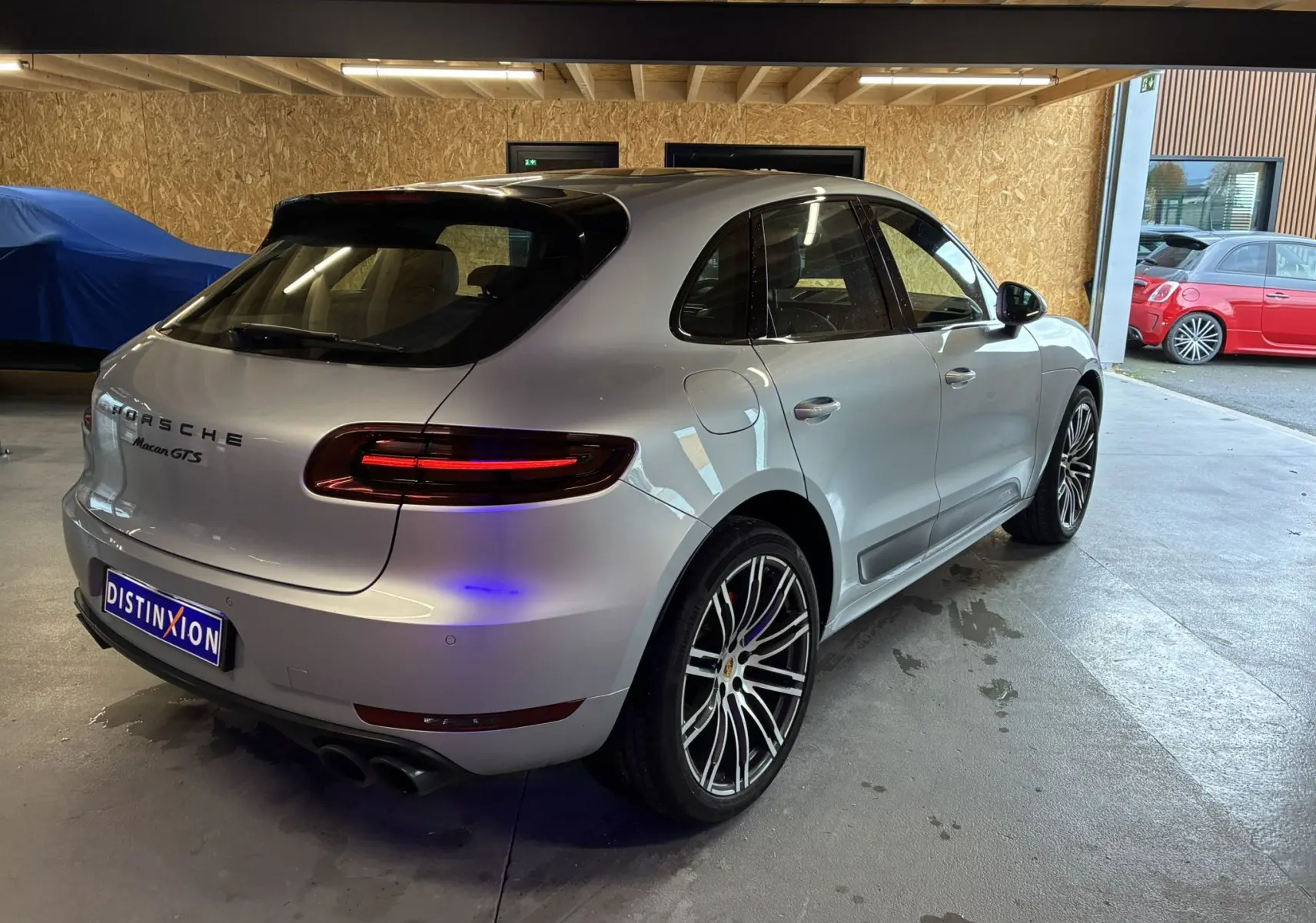 Vue 3/4 arrière droite d'un Porsche Macan GTS gris clair avec jantes RS Spyder 20 pouces en intérieur garage.