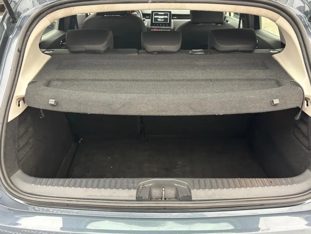 Coffre ouvert vu de l'arrière d'une Renault Clio gris foncé, montrant la plage arrière et les sièges arrière rabattus.