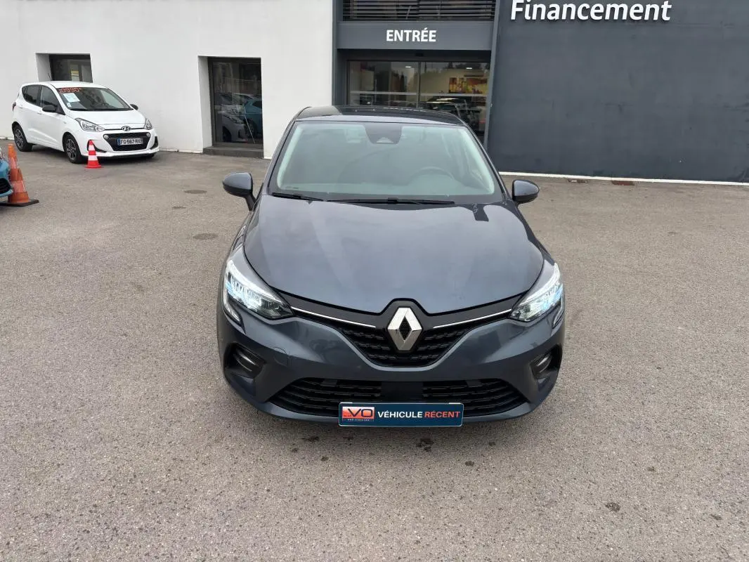 Vue frontale d'une Renault Clio V TCe 90 Equilibre gris foncé avec phares allumés sur un parking extérieur.