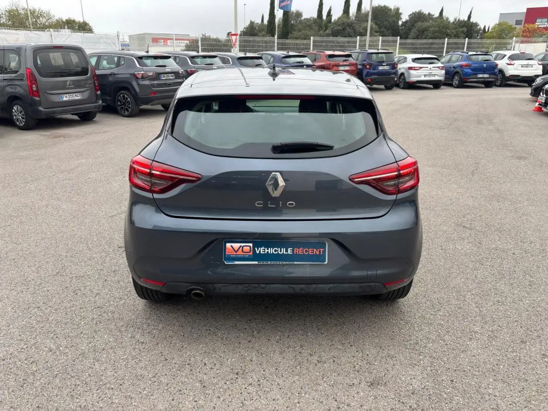 Vue arrière d'une Renault Clio gris foncé 2022, avec feux arrière allumés sur un parking extérieur.
