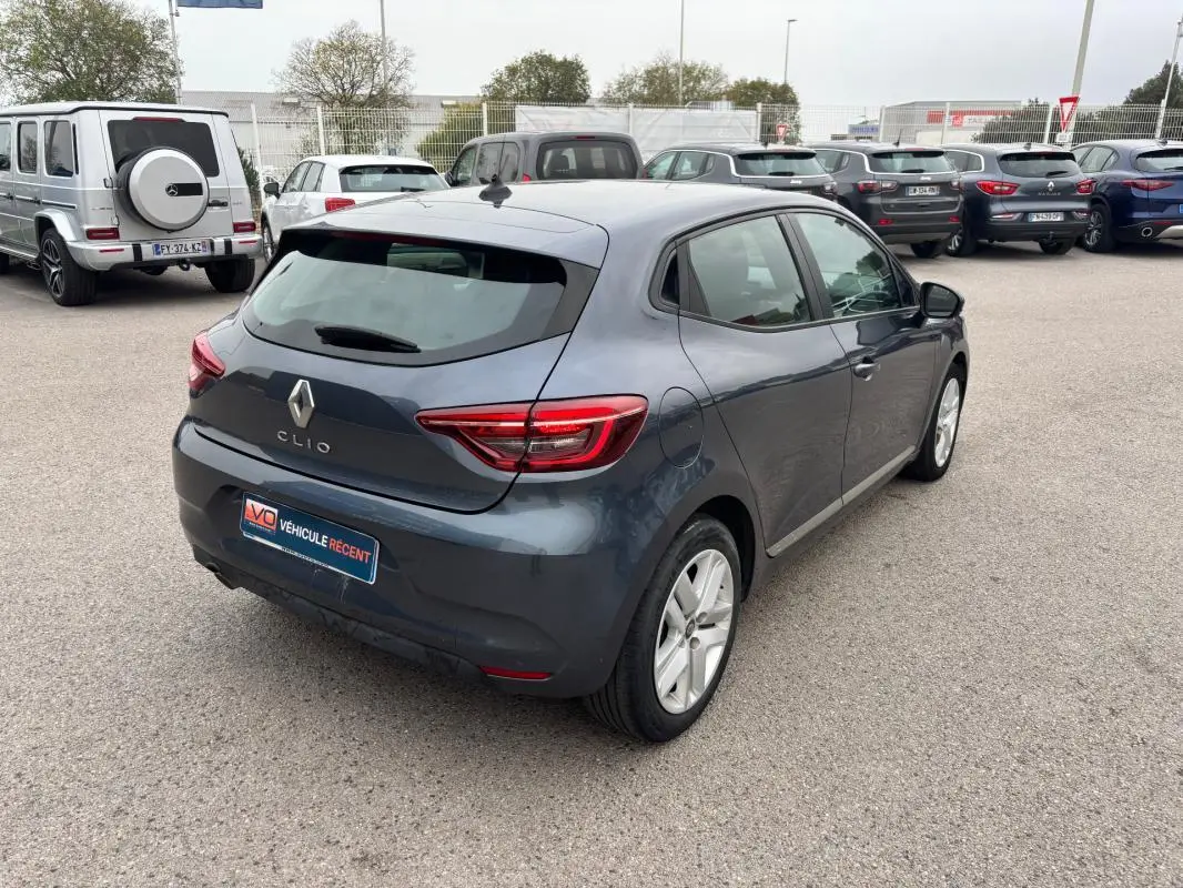 Vue 3/4 arrière droite d'une Renault Clio gris foncé 2022, avec feux arrière allumés sur parking extérieur.
