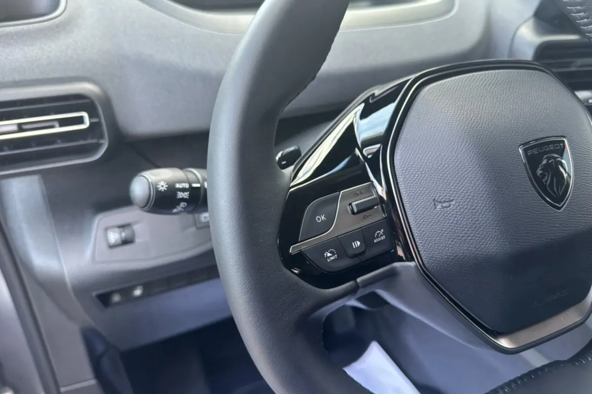 Gros plan sur le volant cuir multifonctions noir du Peugeot Rifter 2026 avec commandes intégrées et logo central.