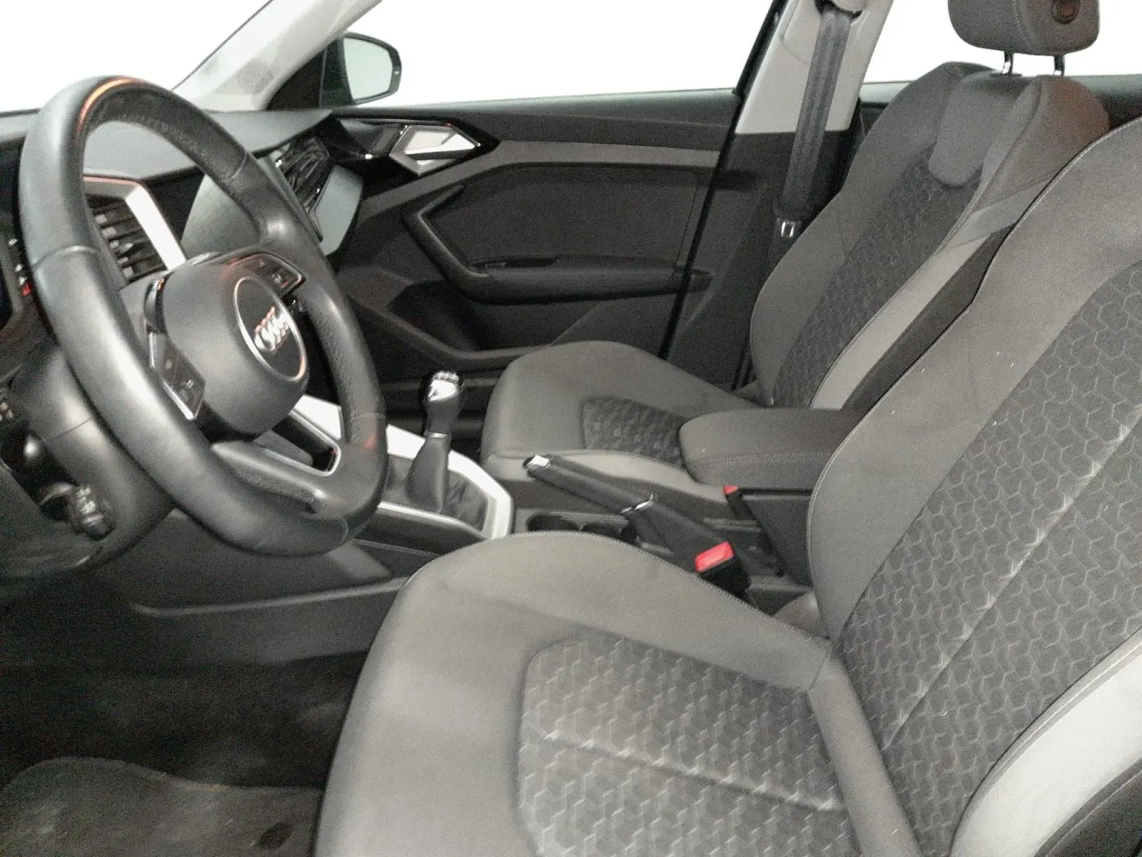 Vue intérieure côté conducteur de l’Audi A1 Sportback 2023, sièges sport gris avec volant cuir et levier de vitesse manuel.