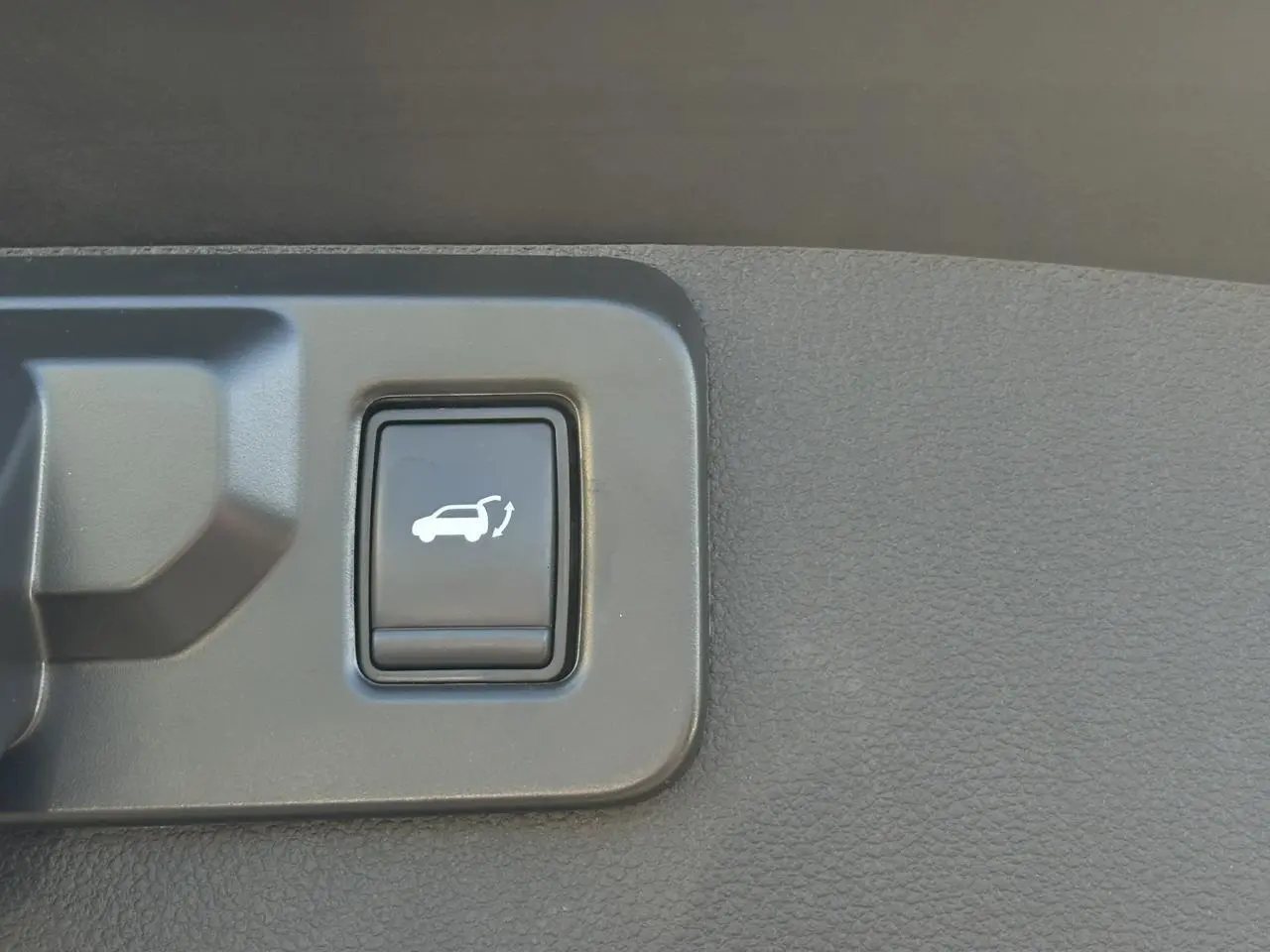 Gros plan sur le bouton d'ouverture du hayon mains libres dans l'habitacle du Renault SYMBIOZ gris Cassiopée.