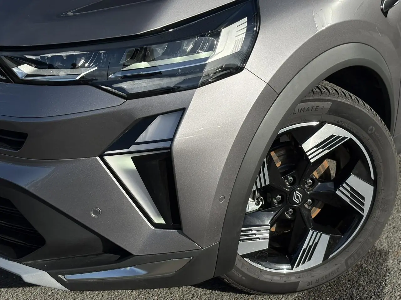 Gros plan sur l'avant droit gris Cassiopée du Renault SYMBIOZ 2025, mettant en valeur le phare LED et la jante 18 pouces.