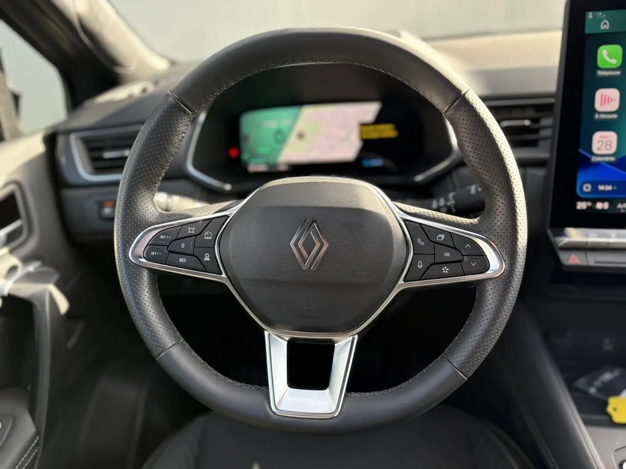 Vue rapprochée du volant noir perforé de la Renault SYMBIOZ 2025 avec commandes intégrées et logo central.