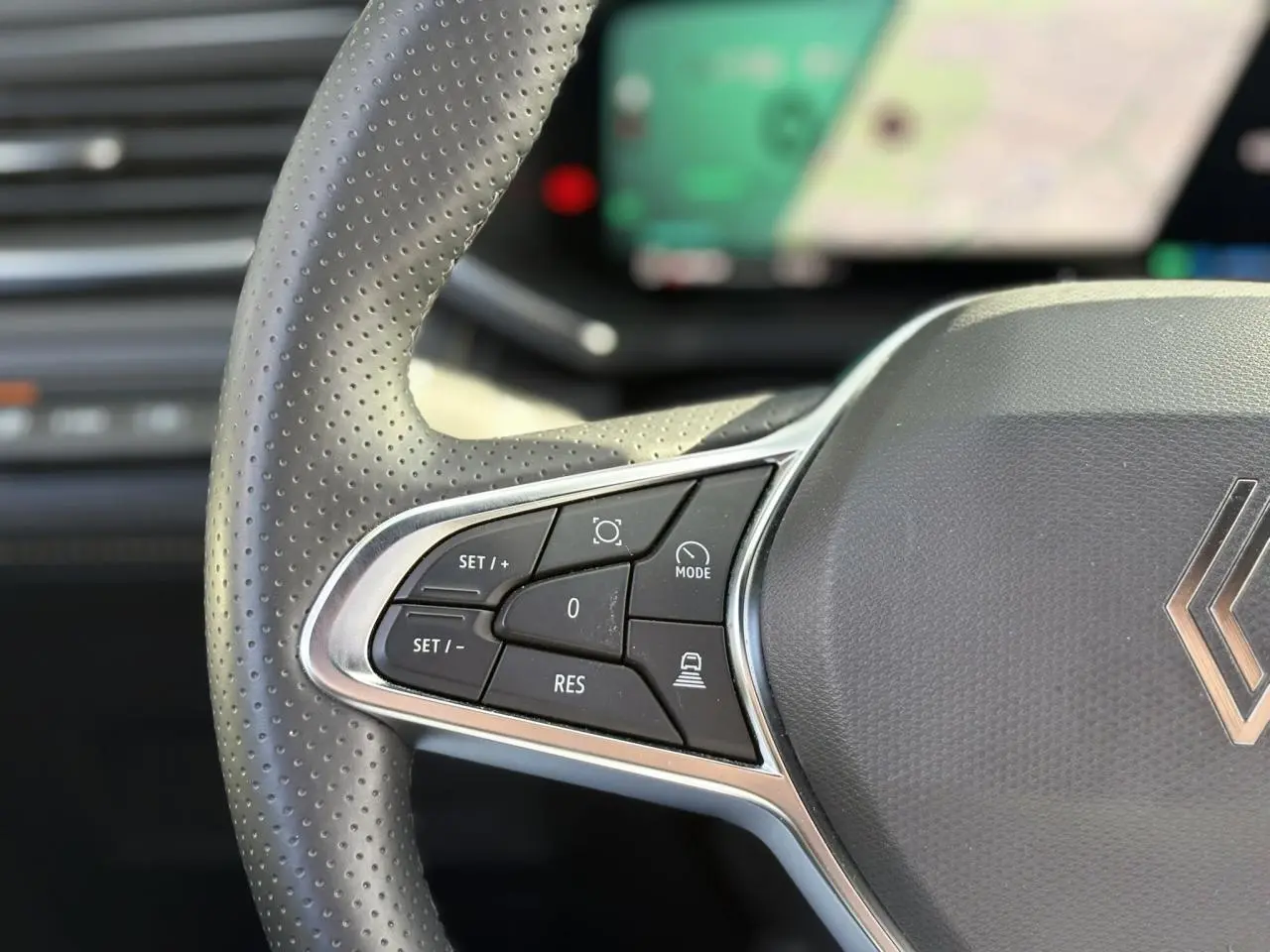 Gros plan sur le côté gauche du volant perforé gris du Renault Symbioz avec commandes de régulateur et assistant de conduite.