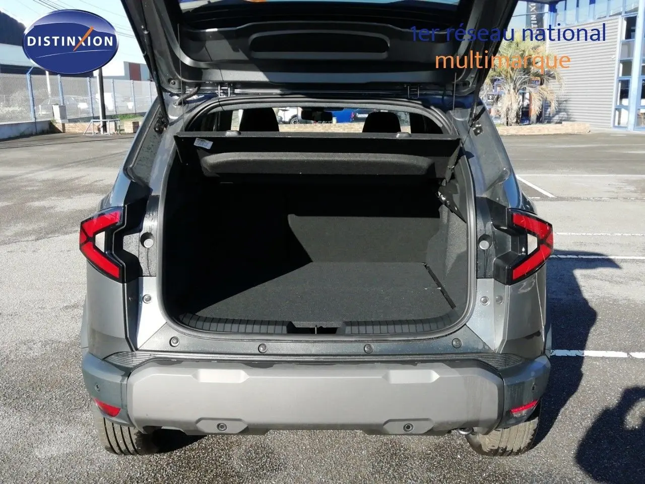 Vue arrière du Dacia Duster gris schiste métal 2026 avec coffre ouvert et feux arrière allumés.