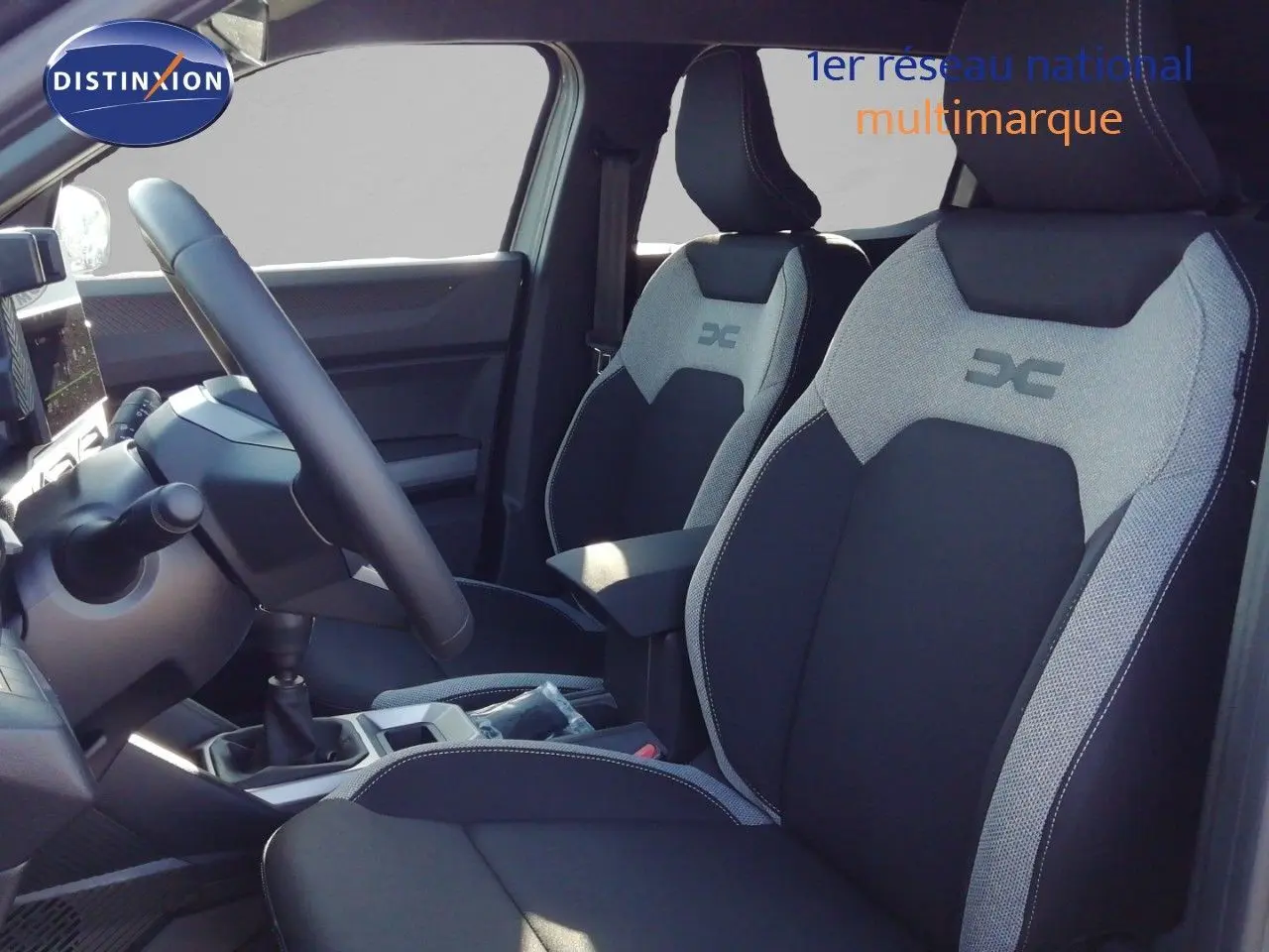 Vue intérieure côté conducteur du Dacia Duster 2026, sièges tissu gris et noir avec logo DC brodé.