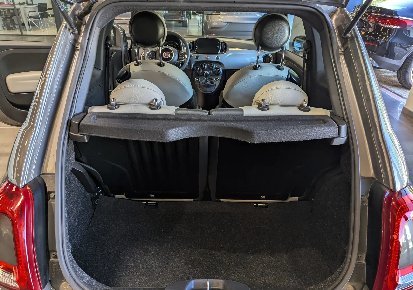 Coffre ouvert d'une Fiat 500 Electroclash Grey 2021, vue arrière montrant l'intérieur clair et le tableau de bord.