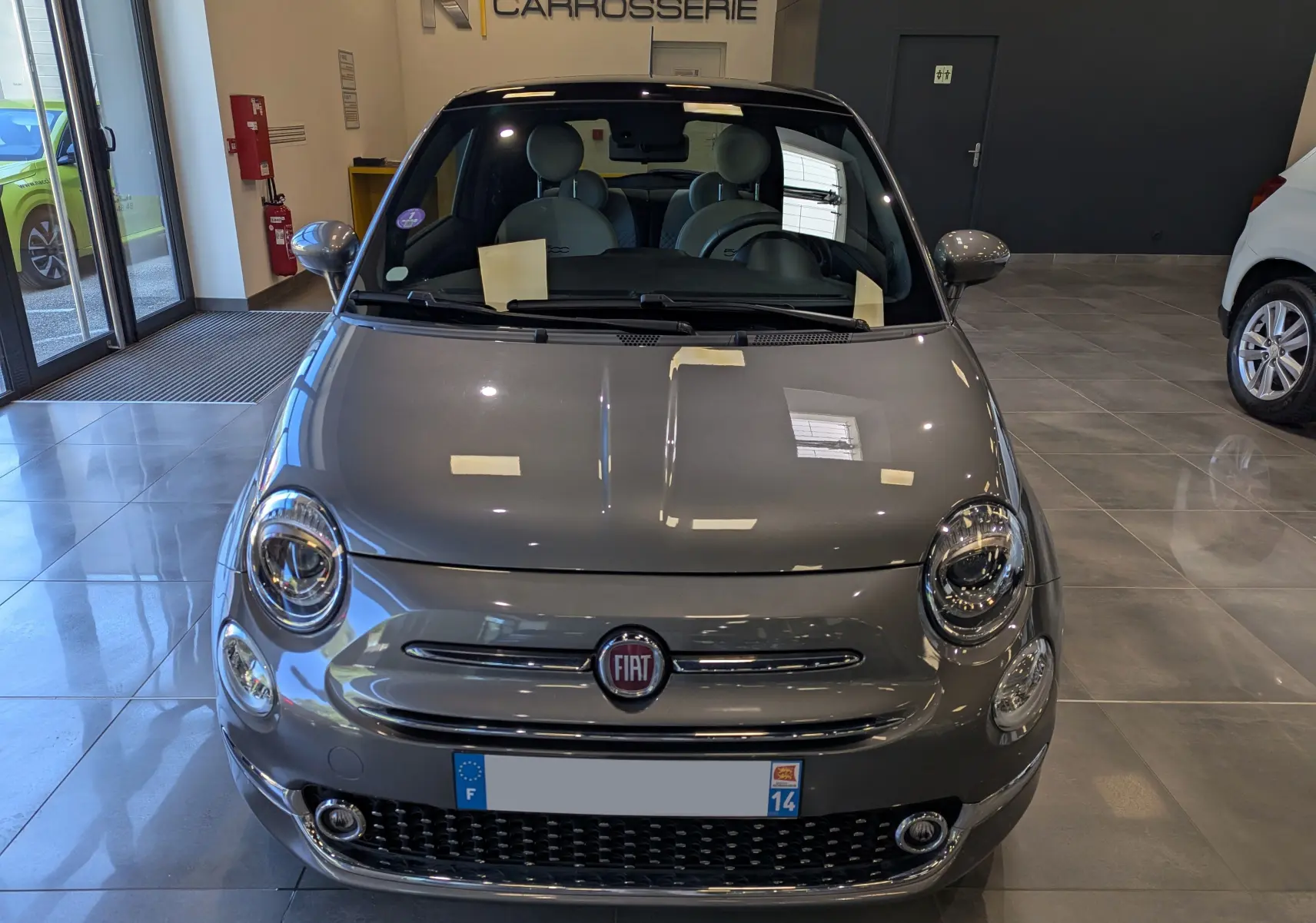 Vue frontale d'une FIAT 500 hybride 2021 en Electroclash Grey, avec phares ronds et calandre chromée dans un showroom.
