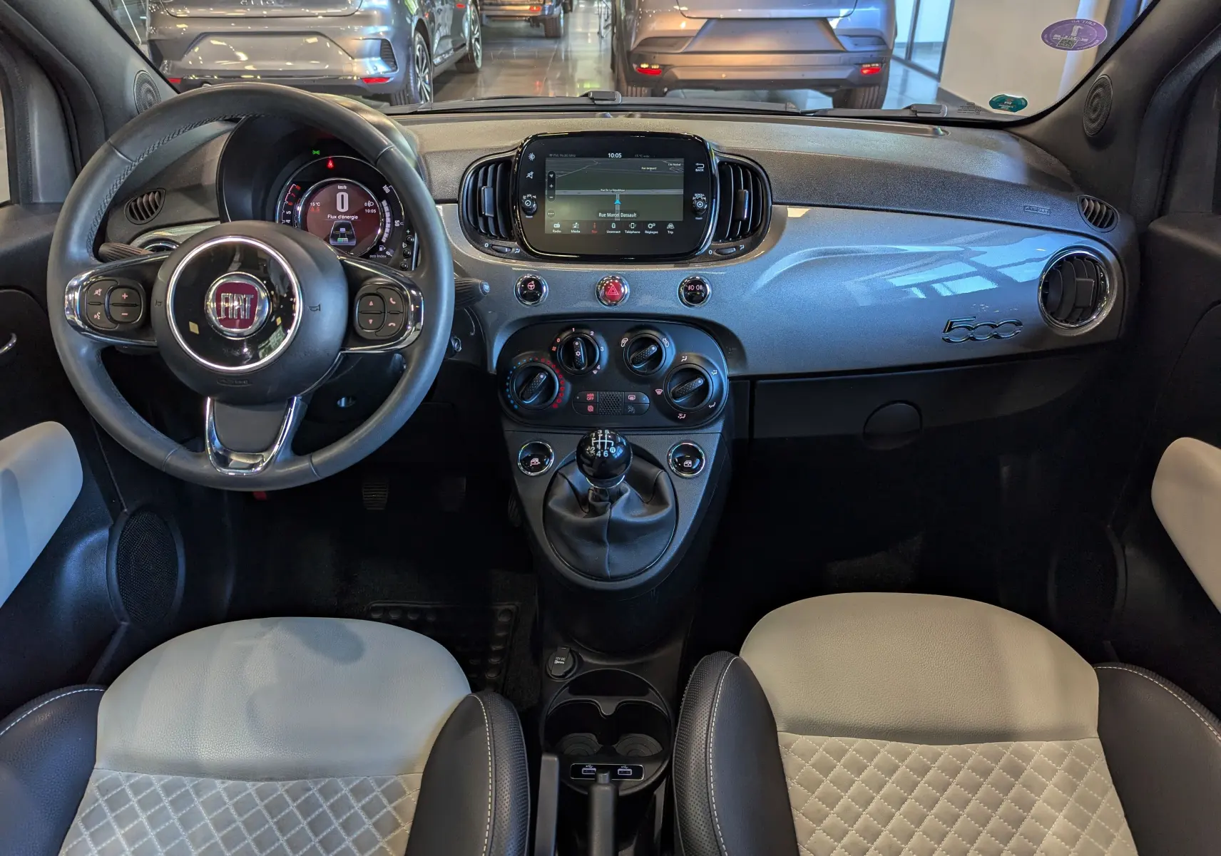 Vue intérieure frontale du tableau de bord gris Electroclash de la Fiat 500 hybride avec volant multifonction et sièges bicolores.