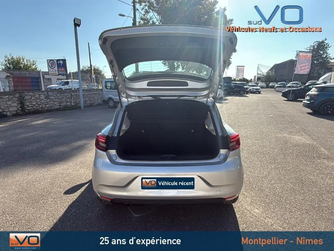 Vue arrière d'une Renault Clio gris clair 2022 avec coffre ouvert sur un parking ensoleillé