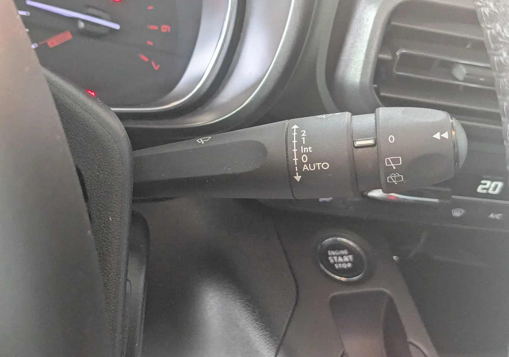 Gros plan sur la commande des essuie-glaces à gauche du volant dans l'habitacle gris noir du Citroën Berlingo beige 2019.