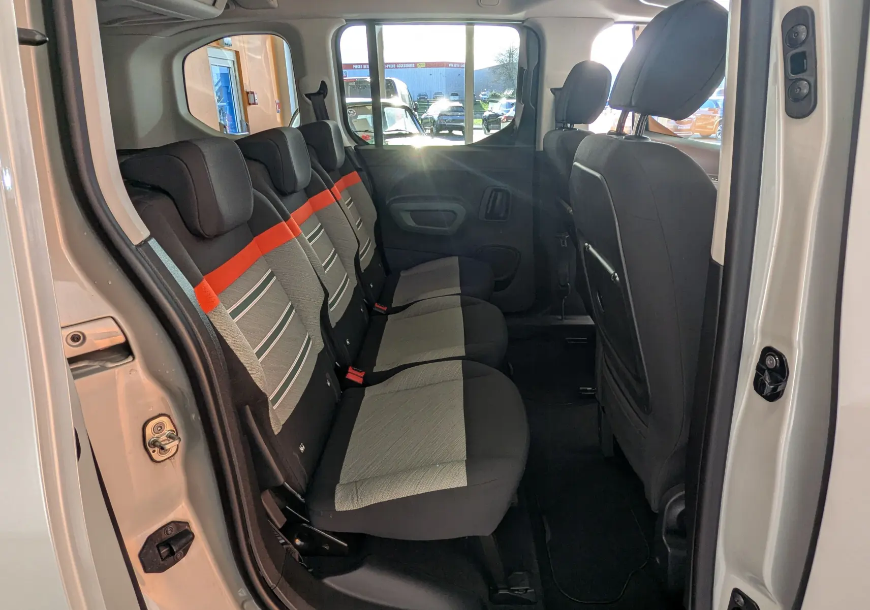 Vue latérale intérieure montrant la banquette arrière grise avec bande orange du Citroën Berlingo beige 2019, portes ouvertes.