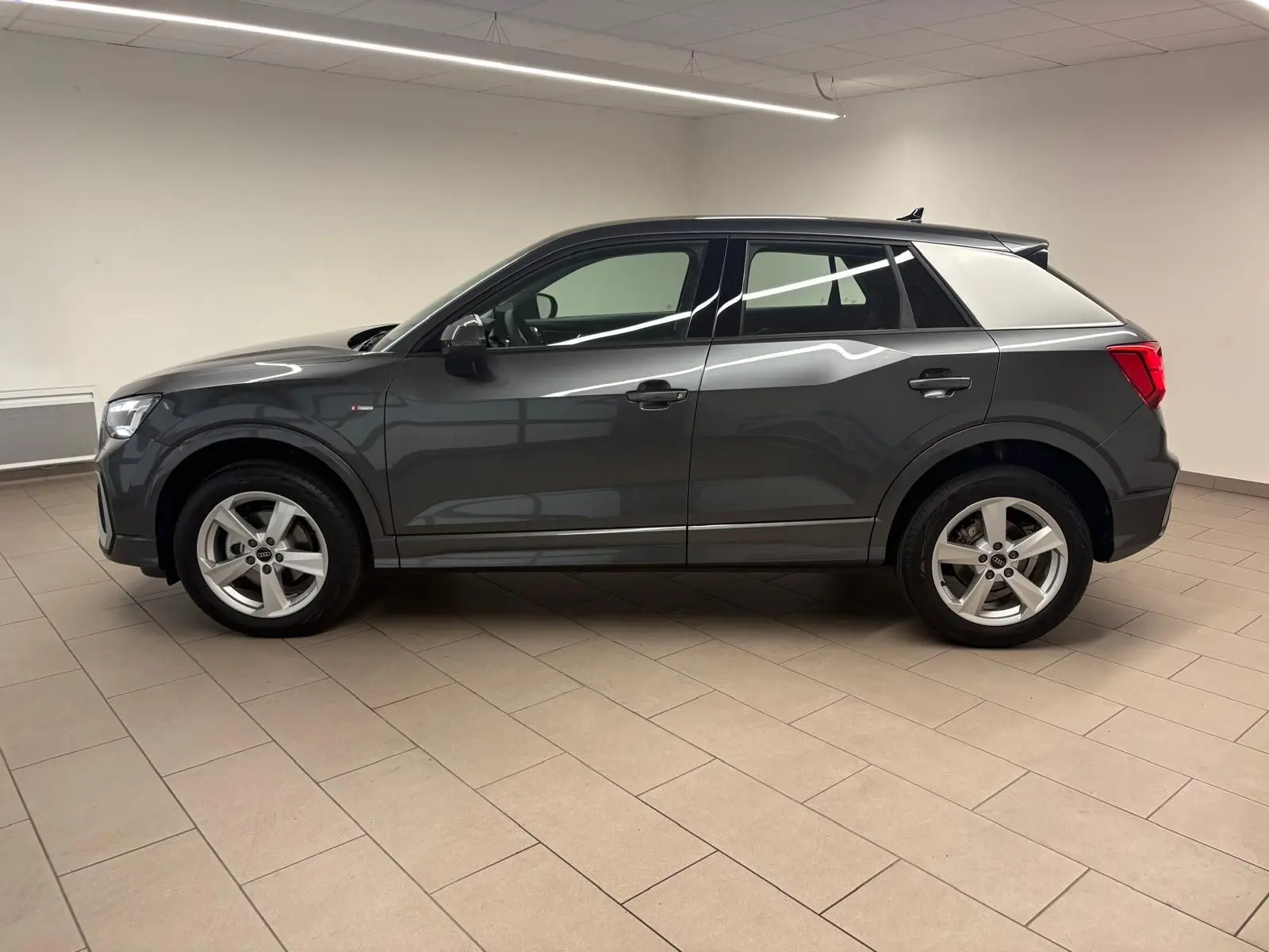 Audi Q2 35 TFSI S Line gris Daytona en profil gauche, avec jantes alliage et toit noir contrasté dans un intérieur neutre.