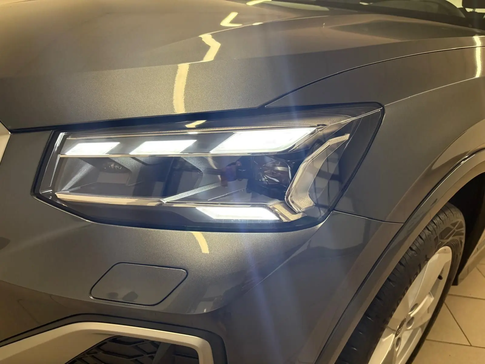 Gros plan sur le phare avant droit allumé d’un Audi Q2 35 TFSI S Line gris Daytona métallisé.