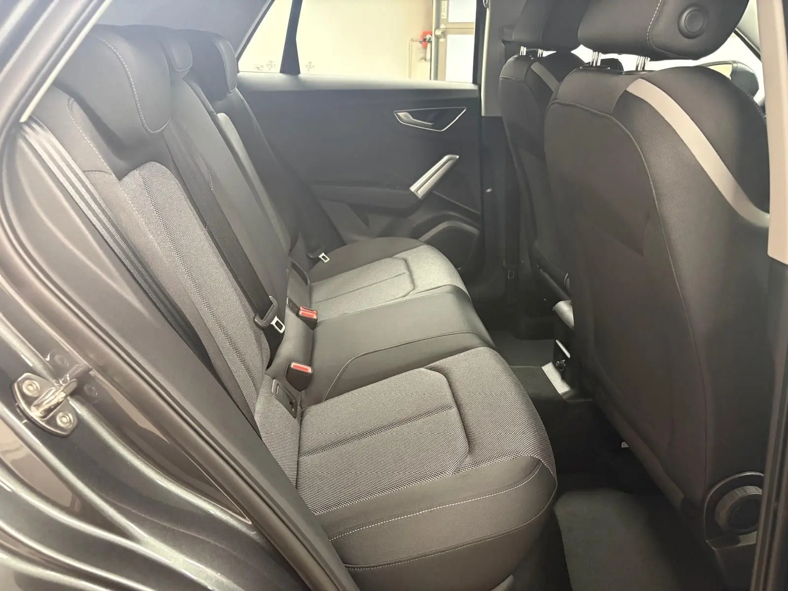 Vue intérieure côté gauche des sièges arrière en tissu gris de l'Audi Q2 35 TFSI S Line 2026 avec portière ouverte.