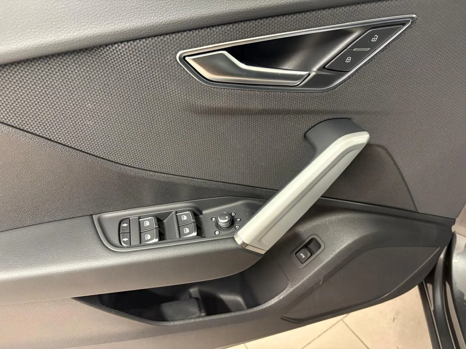 Gros plan sur la porte avant gauche de l’Audi Q2 gris Daytona, montrant les commandes de vitres et la poignée intérieure argentée.