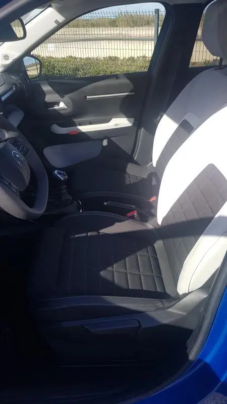 Vue intérieure côté conducteur de la Citroën C3 bleu foncé 2024, sièges bicolores noir et blanc, volant et levier de vitesse visibles.