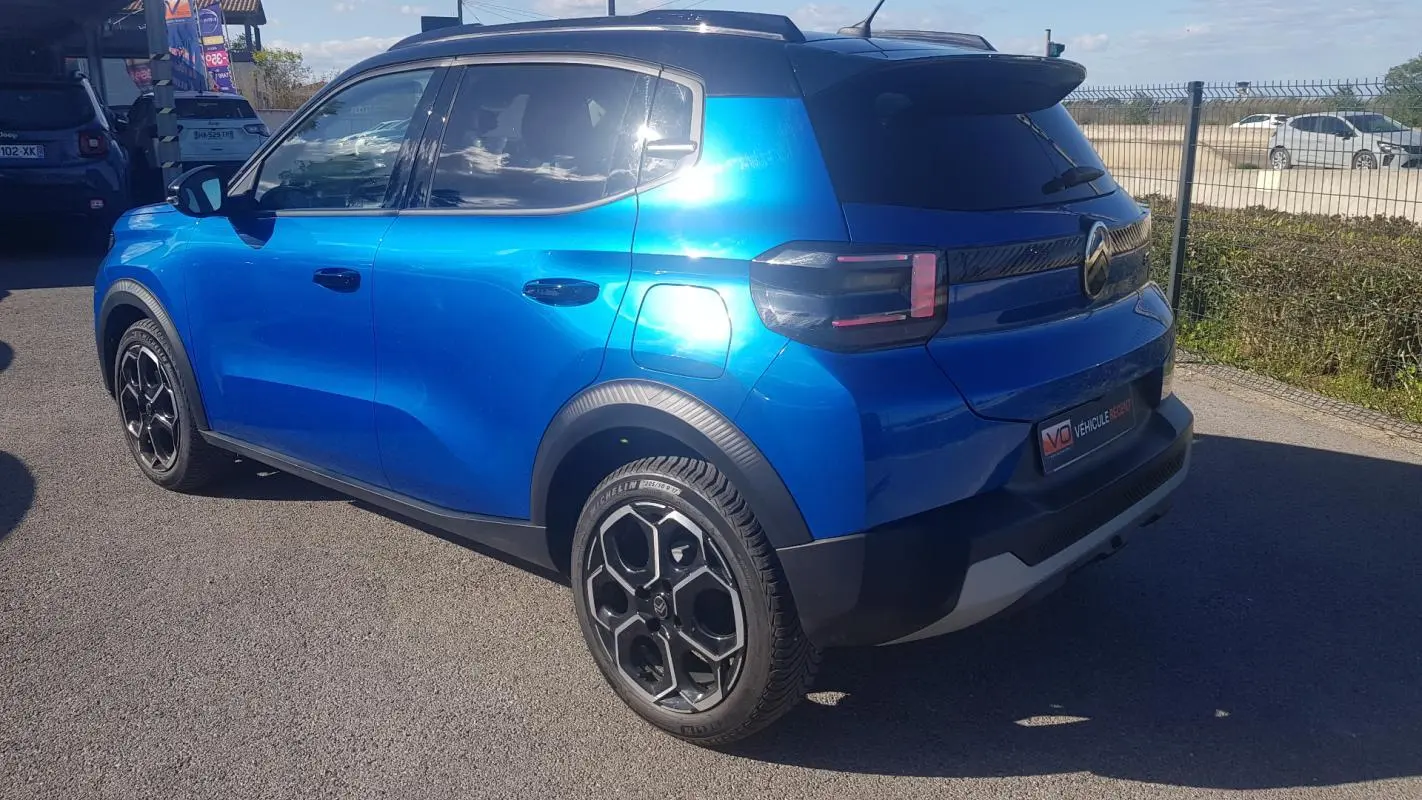Vue 3/4 arrière droite d'une Citroën C3 bleu foncé 2024 avec jantes alliage noires et barres de toit.