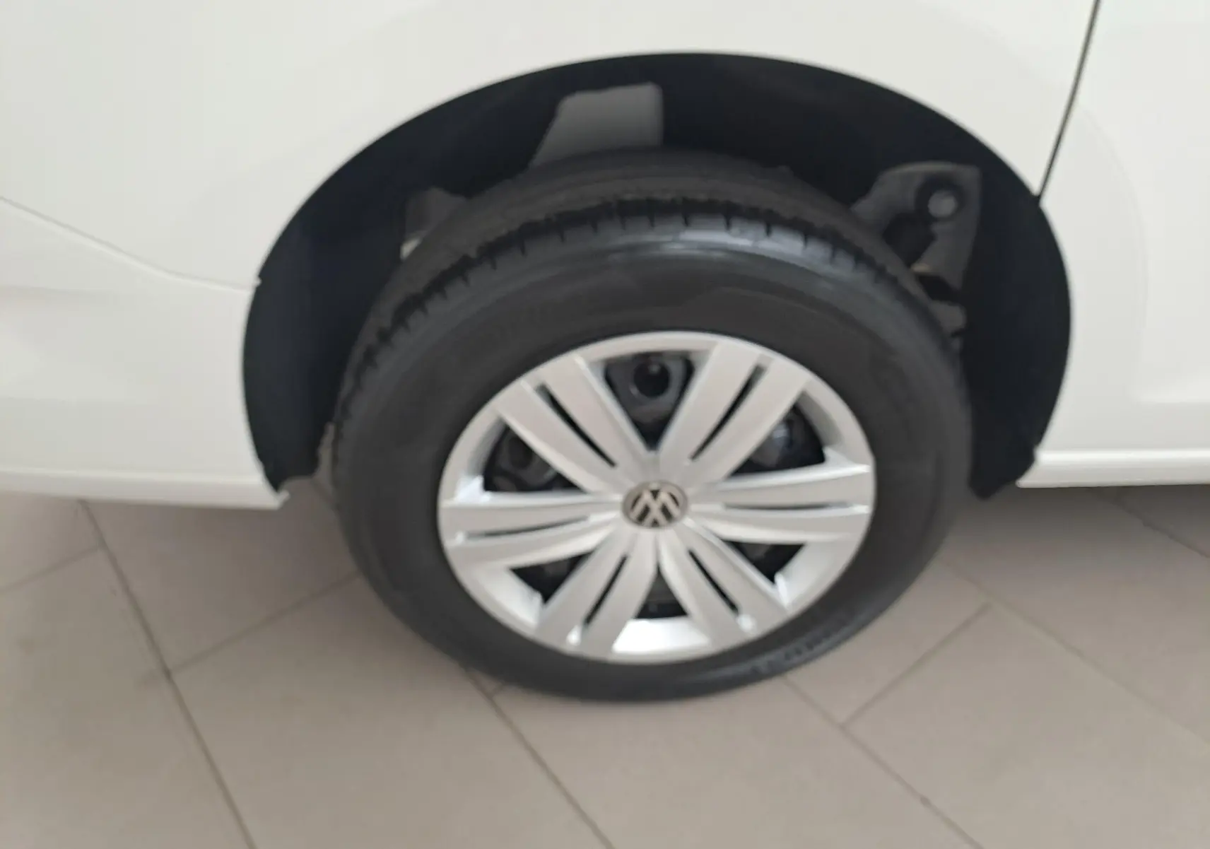 Gros plan sur la roue avant droite d’un Volkswagen Caddy Cargo Maxi blanc Candy avec jante argentée au design moderne.