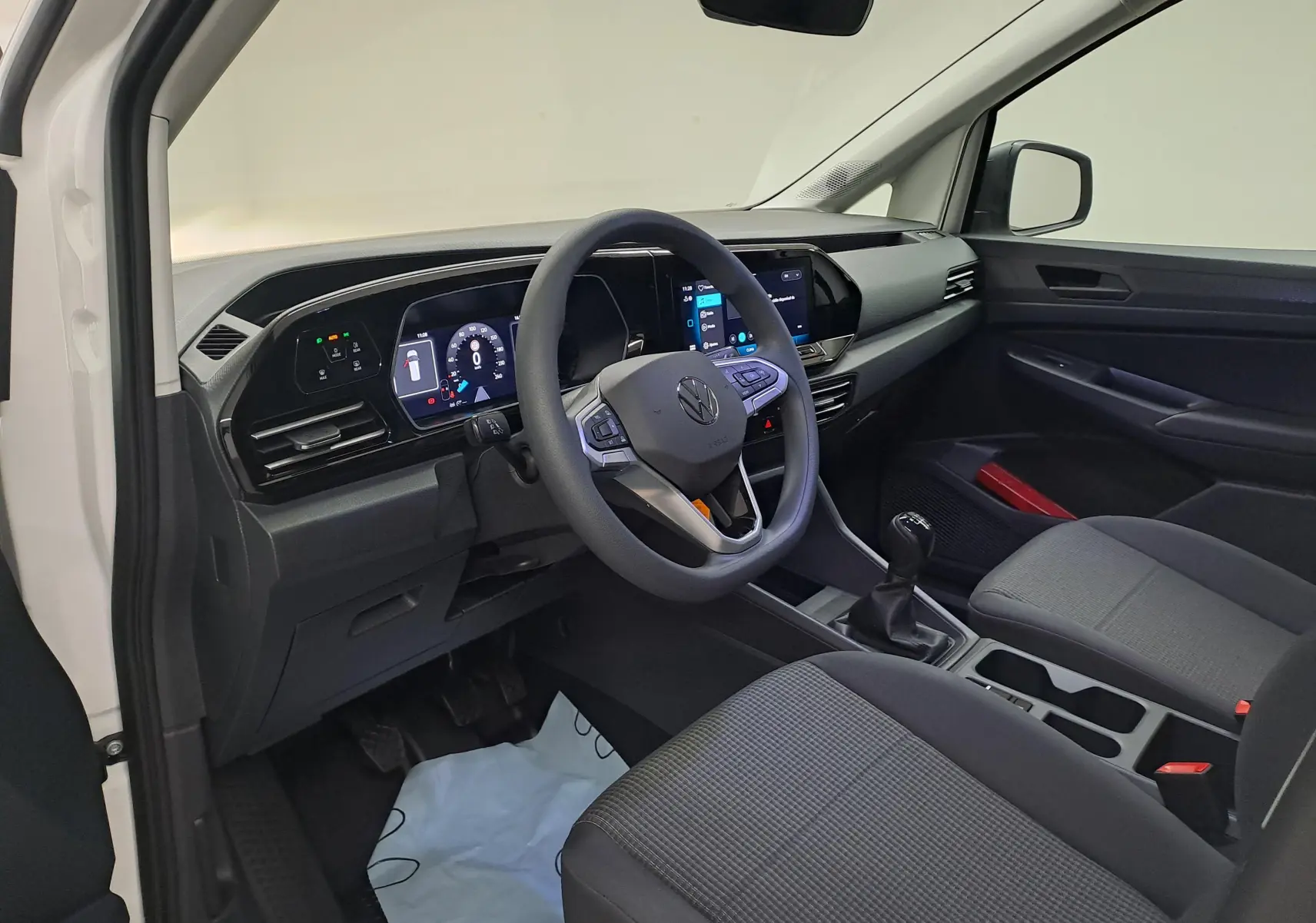 Vue intérieure côté conducteur du Volkswagen Caddy Cargo Maxi 2026 blanc, avec tableau de bord digital et boîte manuelle.