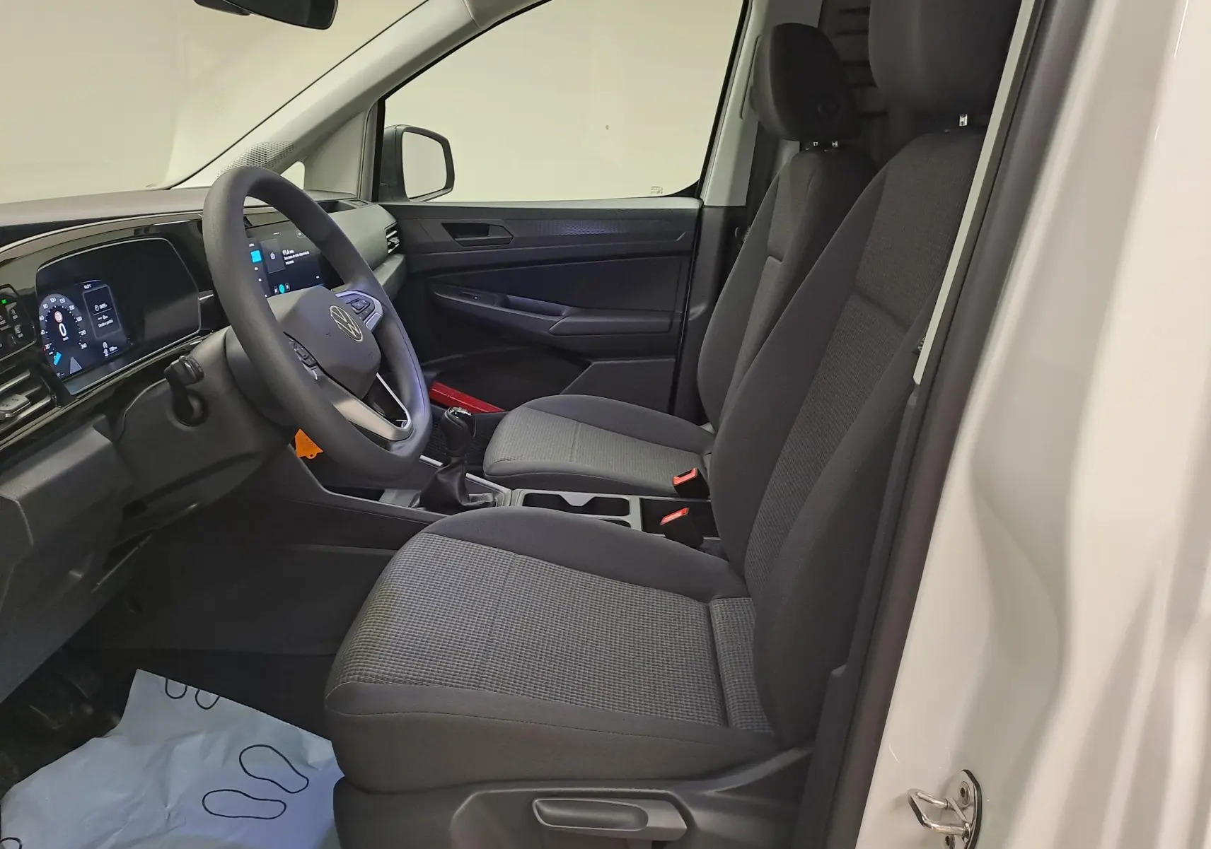Intérieur côté conducteur du Volkswagen Caddy Cargo Maxi blanc, vue de profil montrant sièges noirs et tableau de bord numérique.