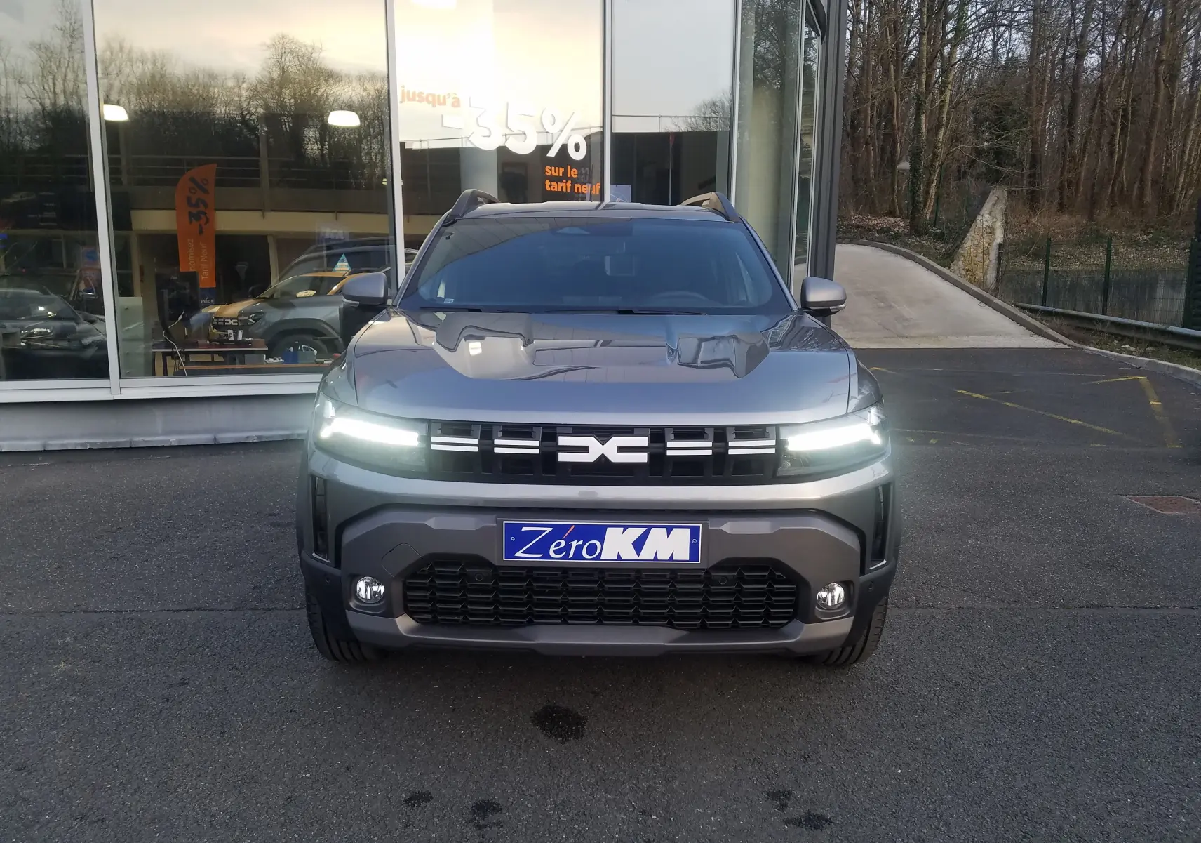 Vue frontale d'un Dacia Duster 2025 gris schiste avec signature lumineuse LED allumée et plaque Zéro KM.