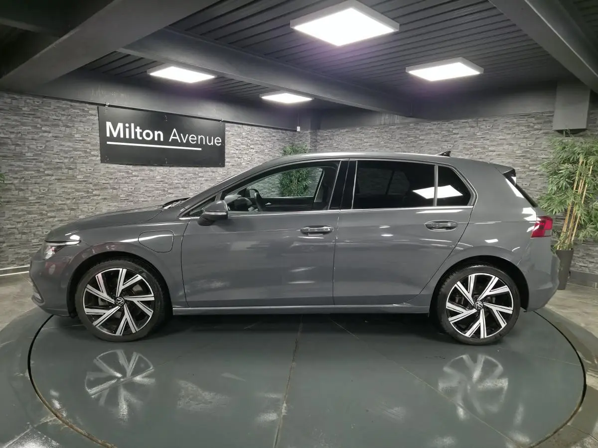 Profil côté gauche d'une Volkswagen Golf gris Urano avec jantes alliage 18 pouces dans un showroom intérieur.