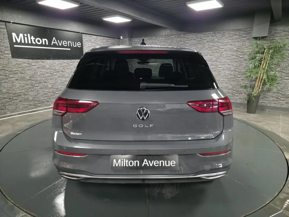 Vue arrière d'une Volkswagen Golf gris Urano hybride rechargeable, avec feux LED et lunette arrière surteintée en intérieur showroom.