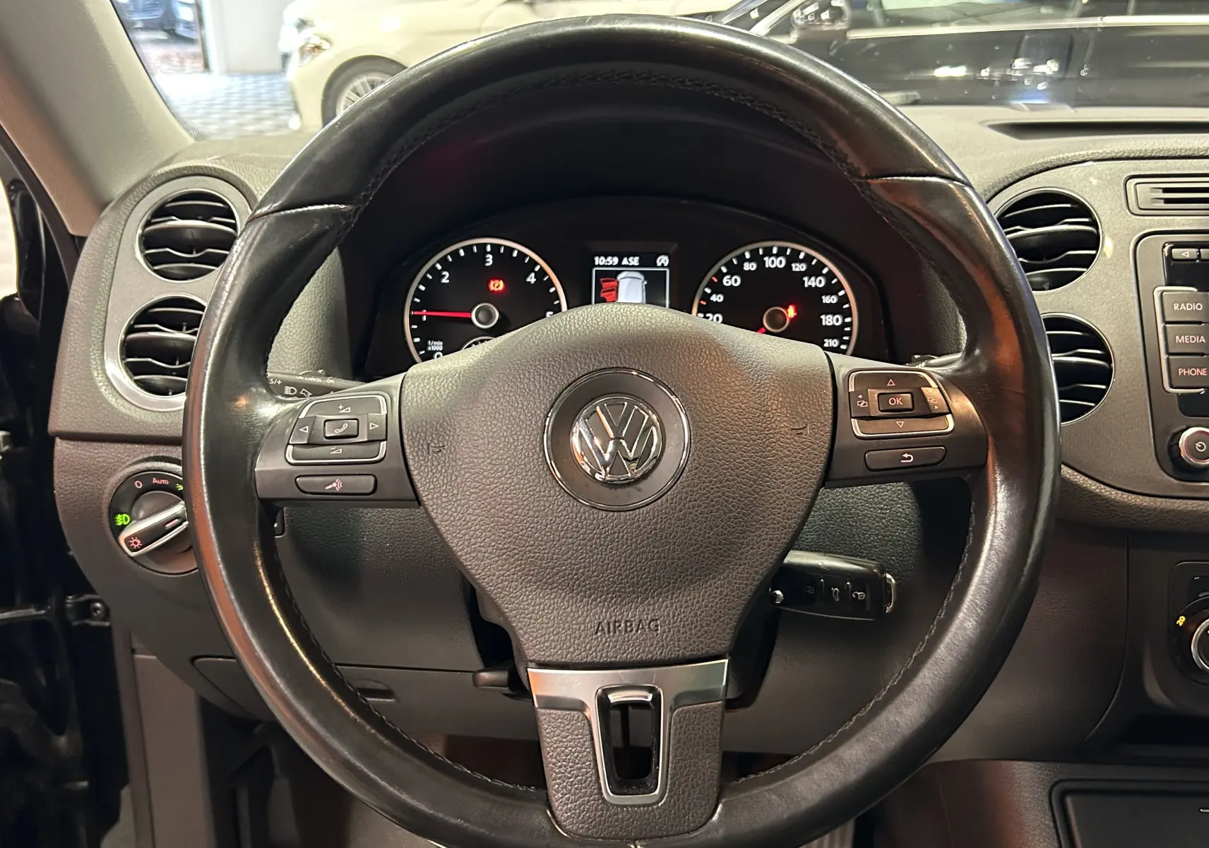 Vue rapprochée du volant en cuir noir du Volkswagen Tiguan 2015 avec commandes intégrées et tableau de bord visible.