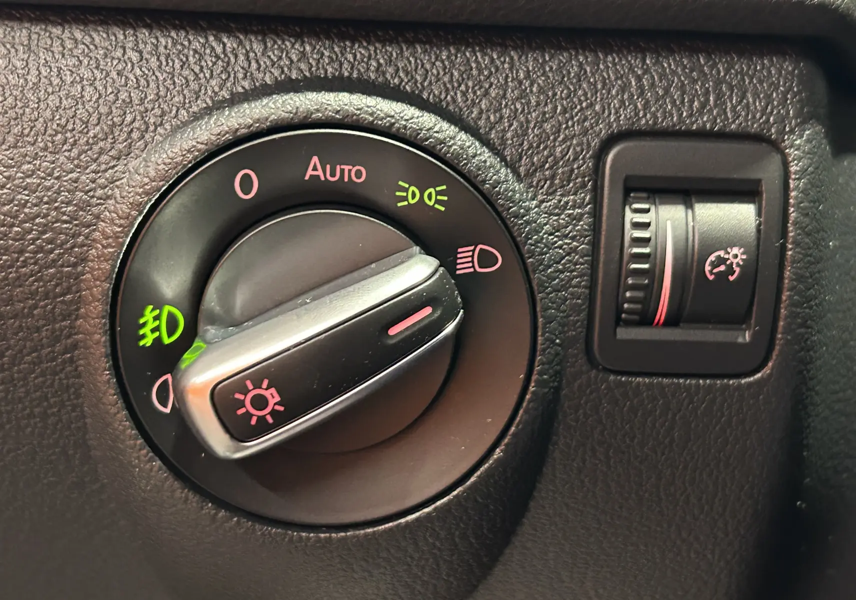 Gros plan sur la molette de réglage des phares et le variateur de luminosité du tableau de bord du Volkswagen Tiguan noir métal.