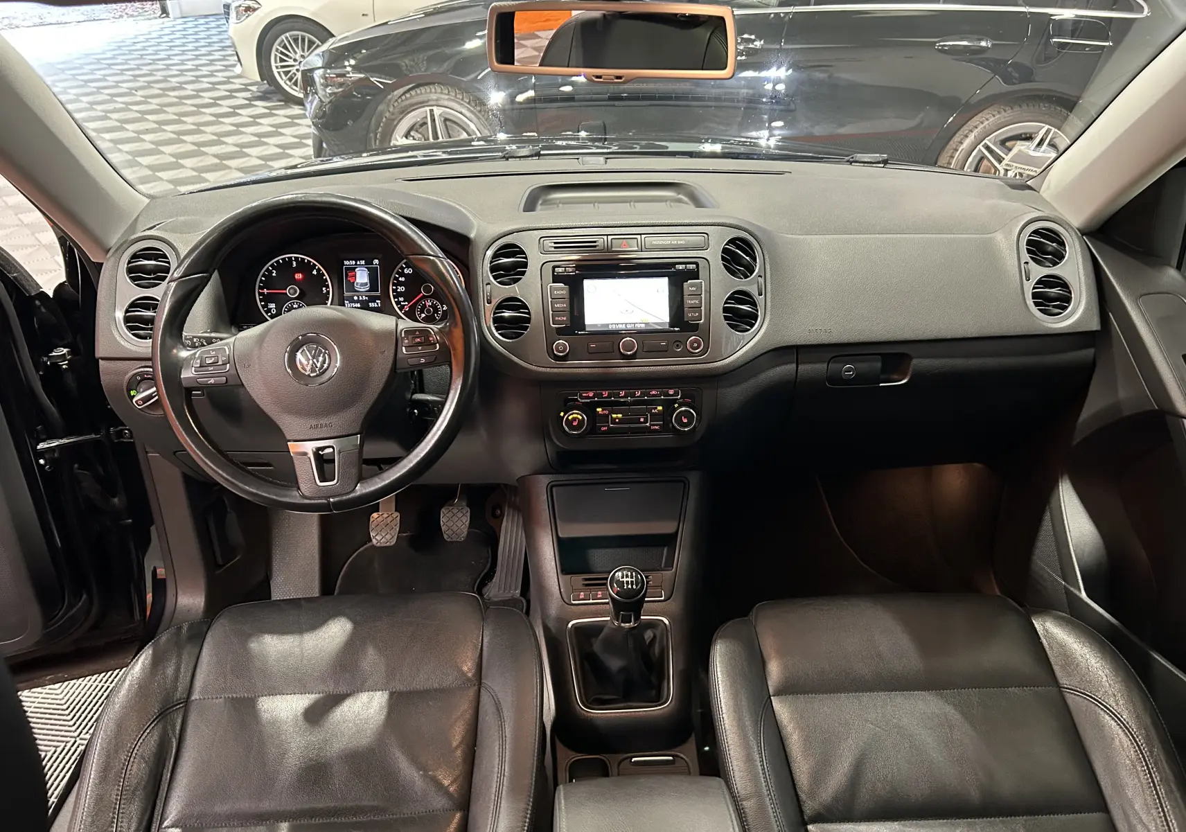 Vue intérieure avant du Volkswagen Tiguan 2.0 TDI 2015 avec sièges cuir noirs, volant multifonction et boîte manuelle.