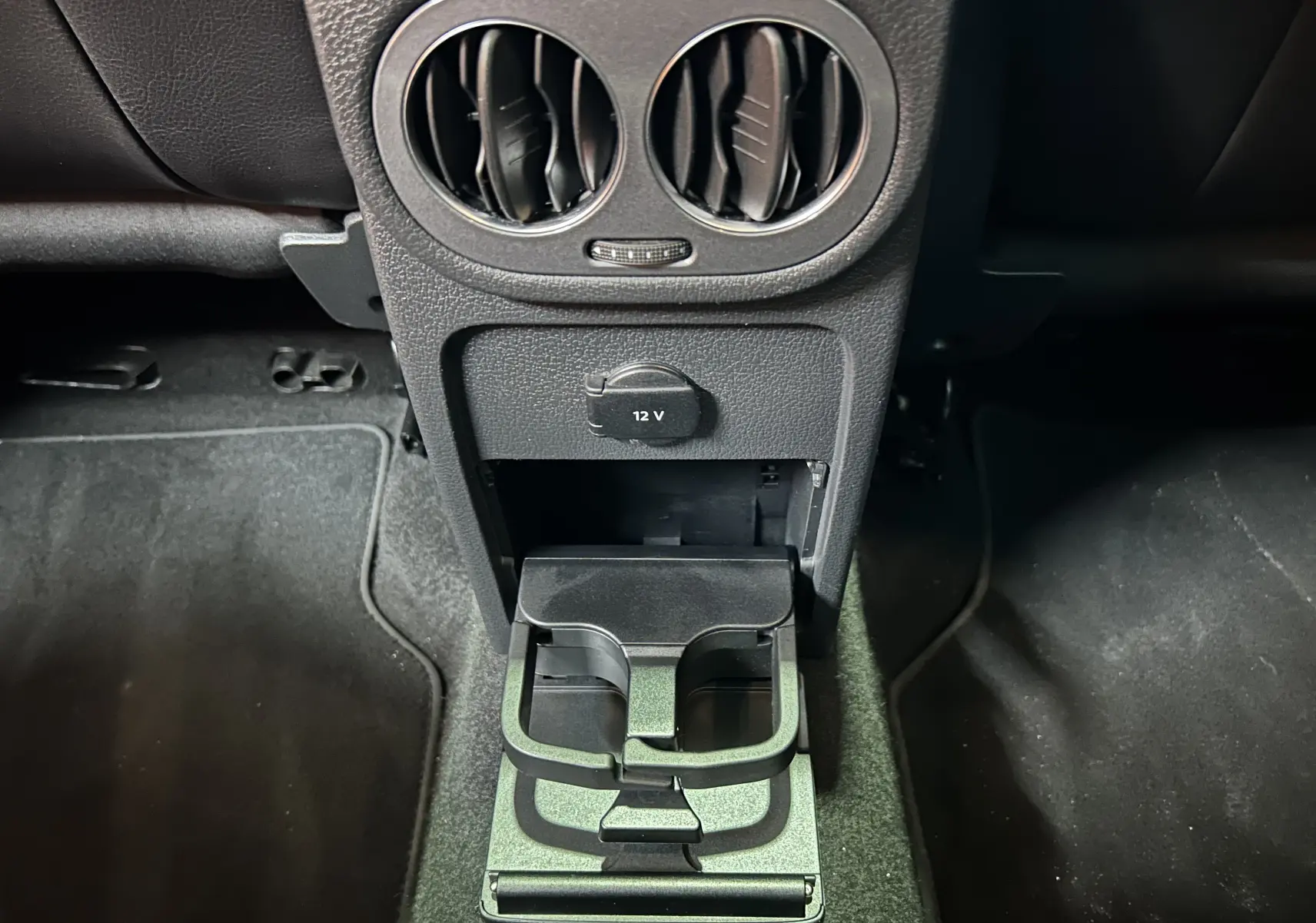 Gros plan sur la console centrale arrière noire du Volkswagen Tiguan 2015, avec porte-gobelets et prise 12V visible.