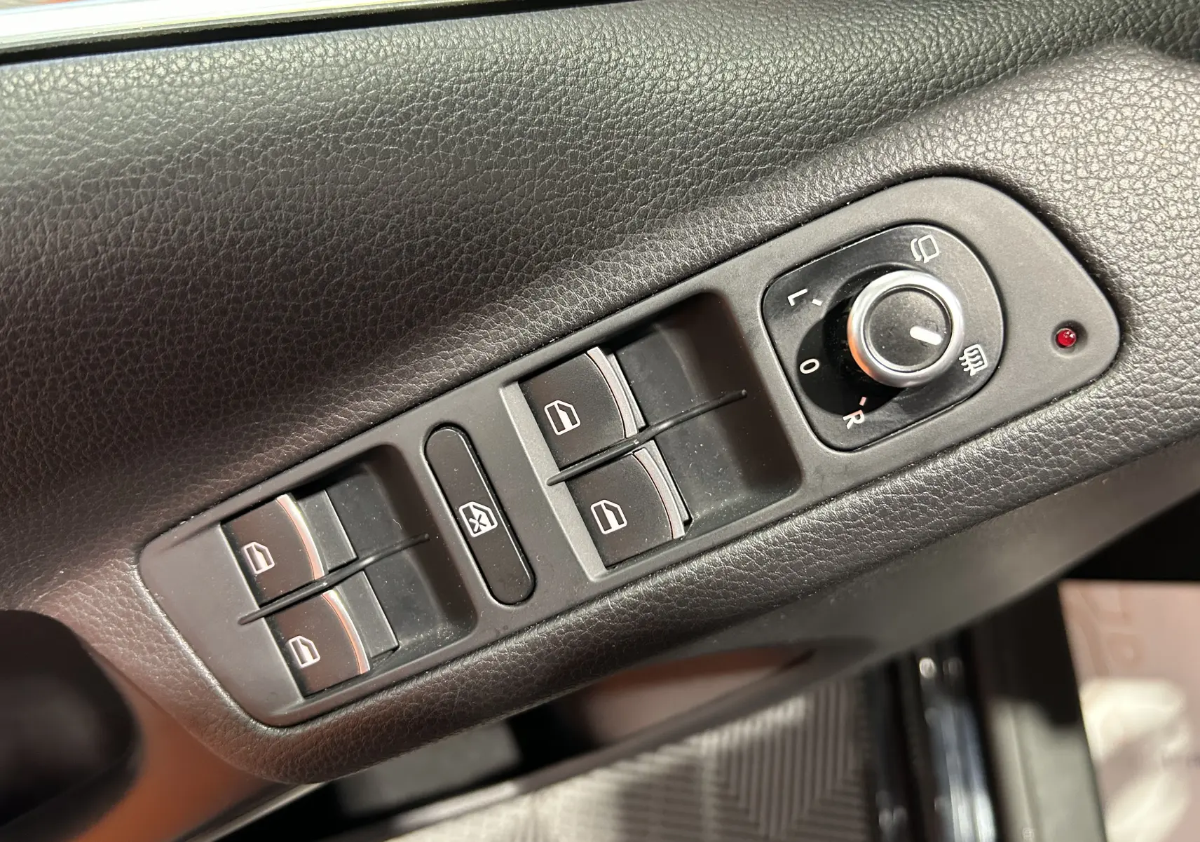 Gros plan sur les commandes de lève-vitres et réglage des rétroviseurs côté conducteur du Volkswagen Tiguan noir métal 2015.