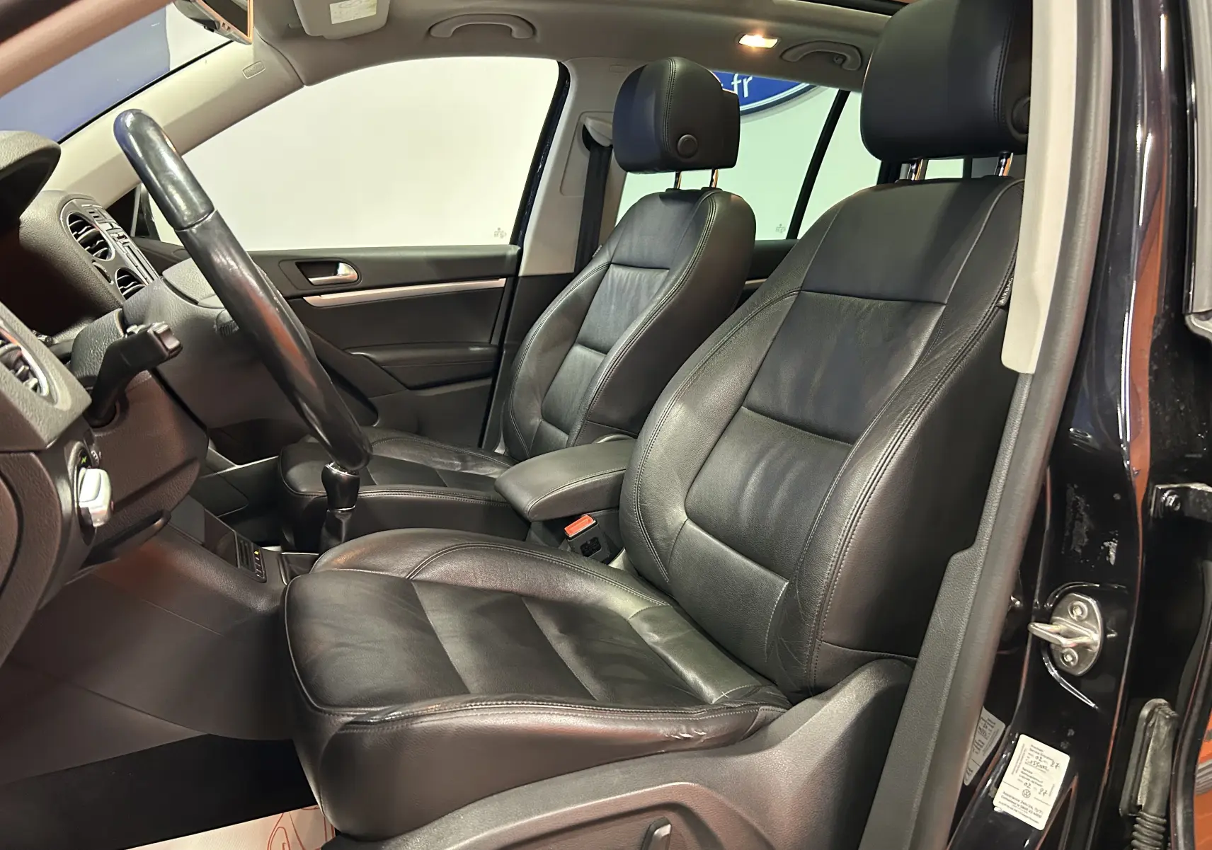 Intérieur noir cuir du Volkswagen Tiguan 2015, vue côté gauche avec sièges avant chauffants et toit ouvrant visible.