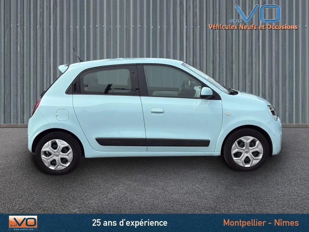 Profil côté gauche d'une Renault Twingo III Zen bleu clair, compacte et urbaine, sur fond industriel neutre.