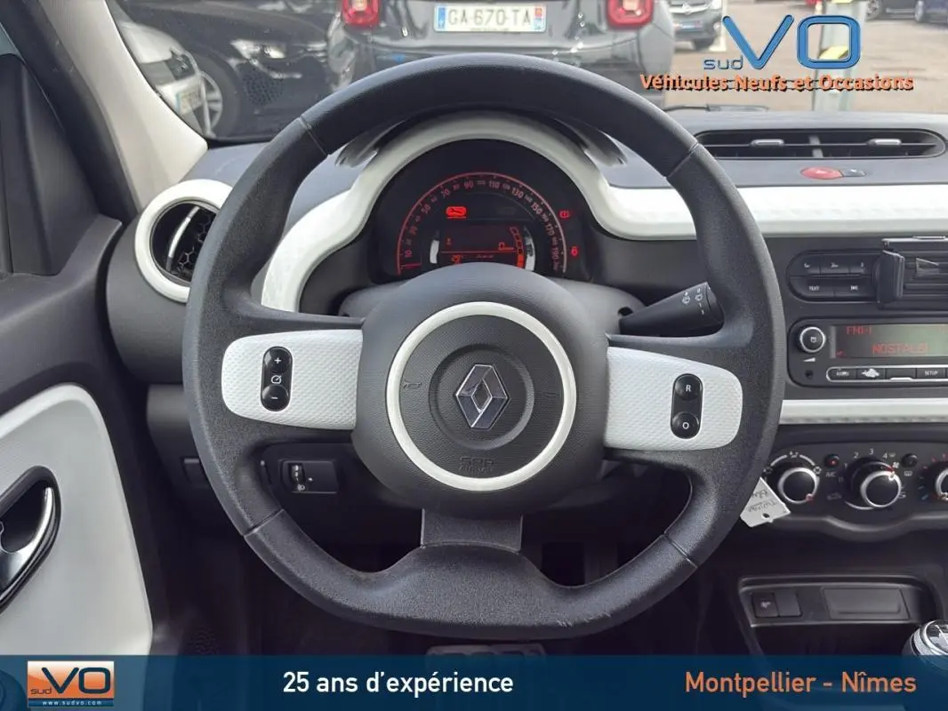 Vue intérieure centrée sur le volant noir et blanc de la Renault Twingo III bleu clair, tableau de bord et commandes visibles.