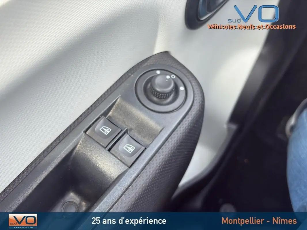 Gros plan sur les commandes des vitres électriques et réglage des rétroviseurs côté conducteur d'une Renault Twingo III bleu clair.