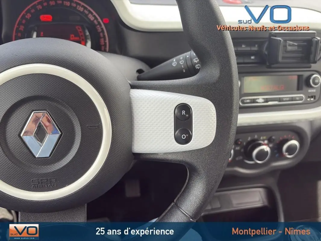 Vue rapprochée du volant noir et blanc de la Renault Twingo III bleu clair avec tableau de bord et commandes visibles.