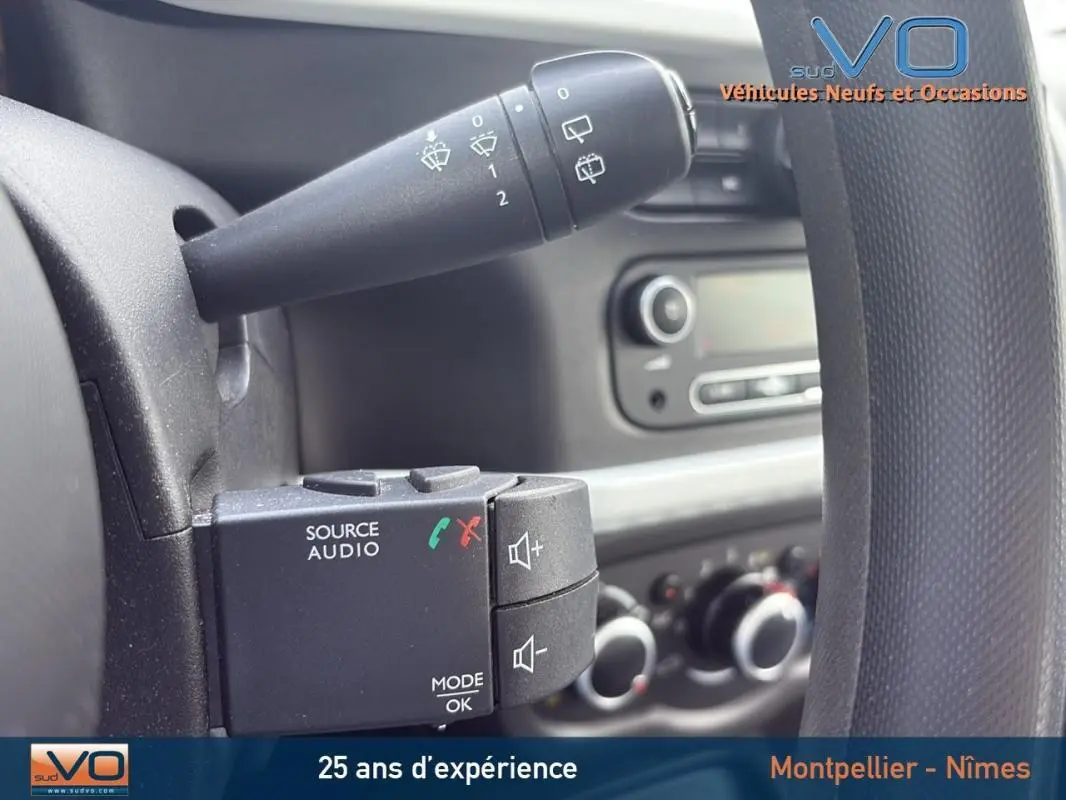 Gros plan sur la commande audio au volant d'une Renault Twingo III bleu clair, avec tableau de bord en arrière-plan.