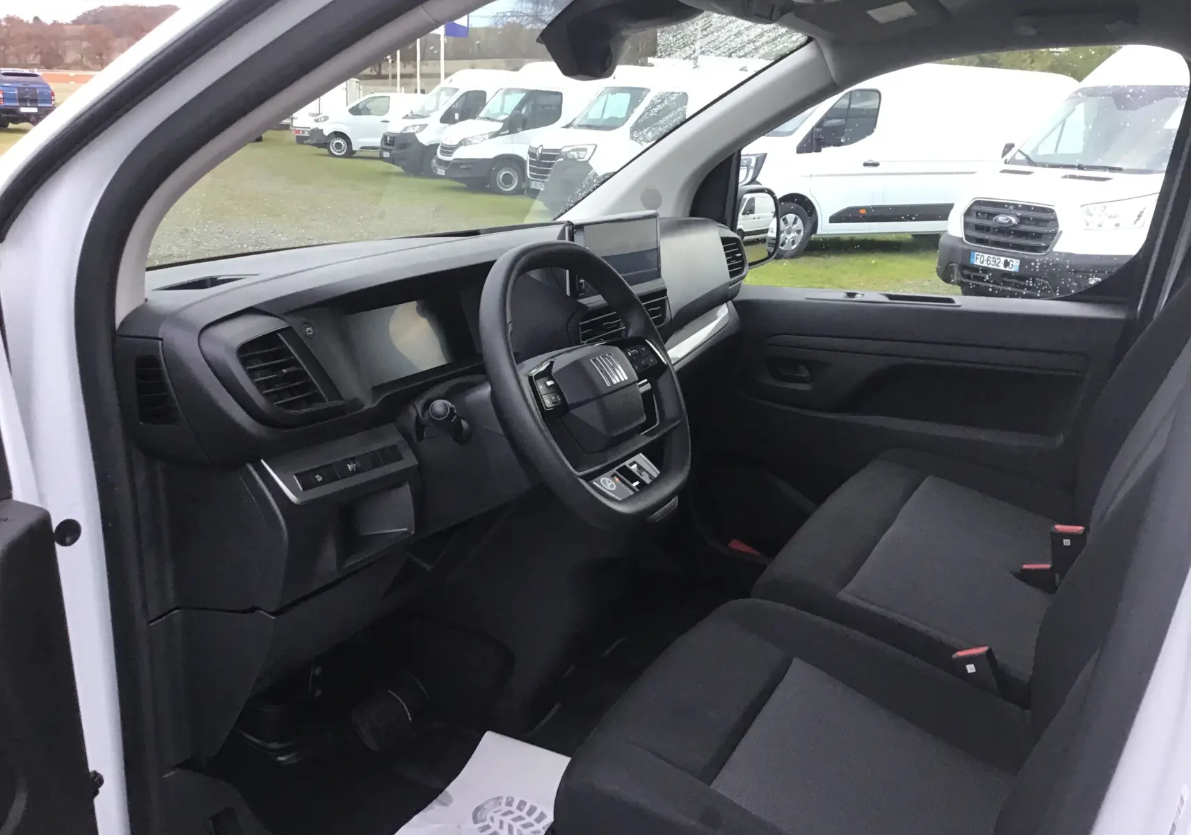 Vue intérieure côté conducteur du Fiat Scudo Fourgon blanc 2024, montrant le tableau de bord moderne et les sièges noirs.